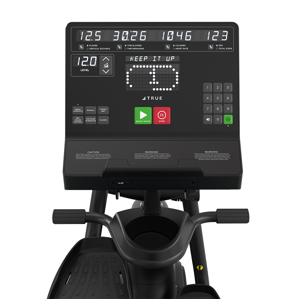 Close-up of a digital display panel on a stationary exercise machine, showing workout stats like time, distance, speed, calories, and heart rate, with various buttons and a KEEP IT UP message visible on the screen.