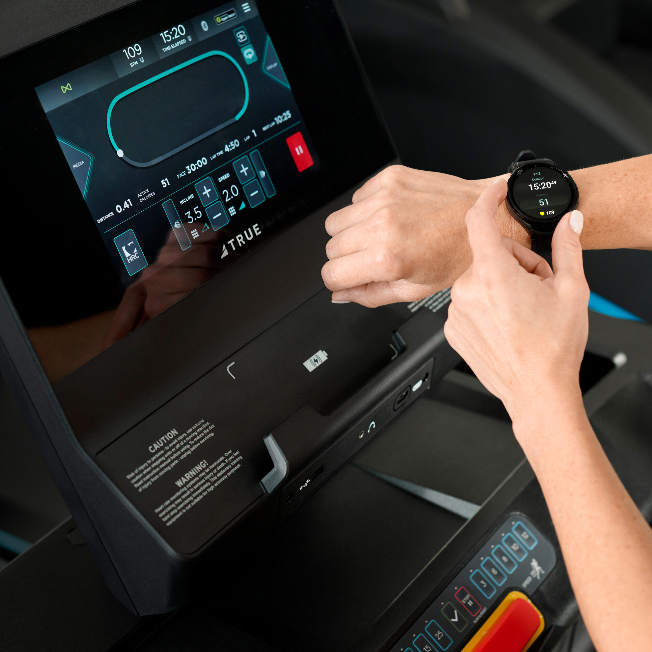 A person checks their smartwatch while using a treadmill, which displays workout data on its screen. The treadmill control panel and the person’s hands are clearly visible.
