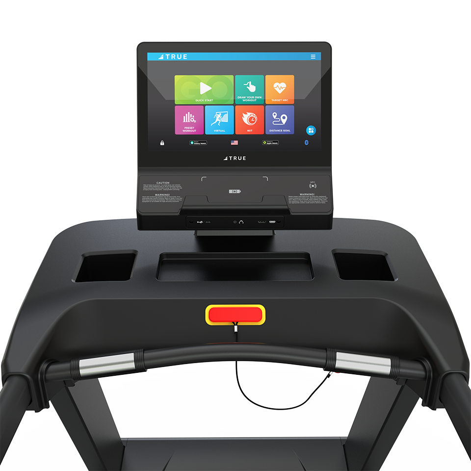 Close-up of a treadmill console with a large touchscreen display showing colorful fitness app icons. The treadmill has a safety key with a red stripe and built-in storage compartments on the panel.