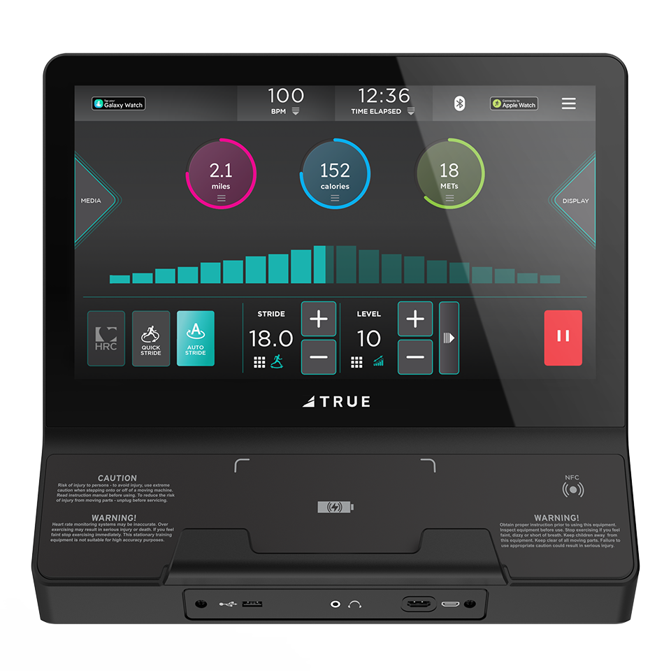 A treadmill console display showing workout stats: 100 BPM heart rate, 12:36 elapsed time, 2.1 miles distance, 152 calories burned, 18 METs, and control buttons. Brand name TRUE is visible.