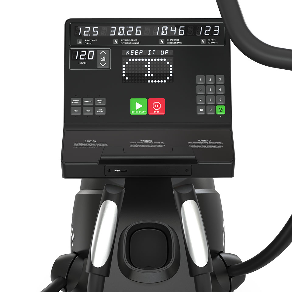 Close-up of a digital exercise machine console showing a display with workout stats, buttons for level and control, and an encouraging message reading KEEP IT UP in white LED dots.