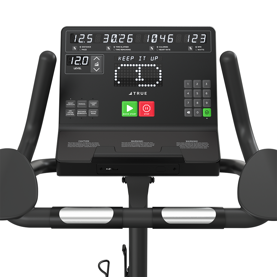 Close-up of the control panel of a stationary exercise bike, displaying digital metrics such as time, distance, calories, and speed, with buttons for start, stop, and workout level, and handlebars visible on both sides.