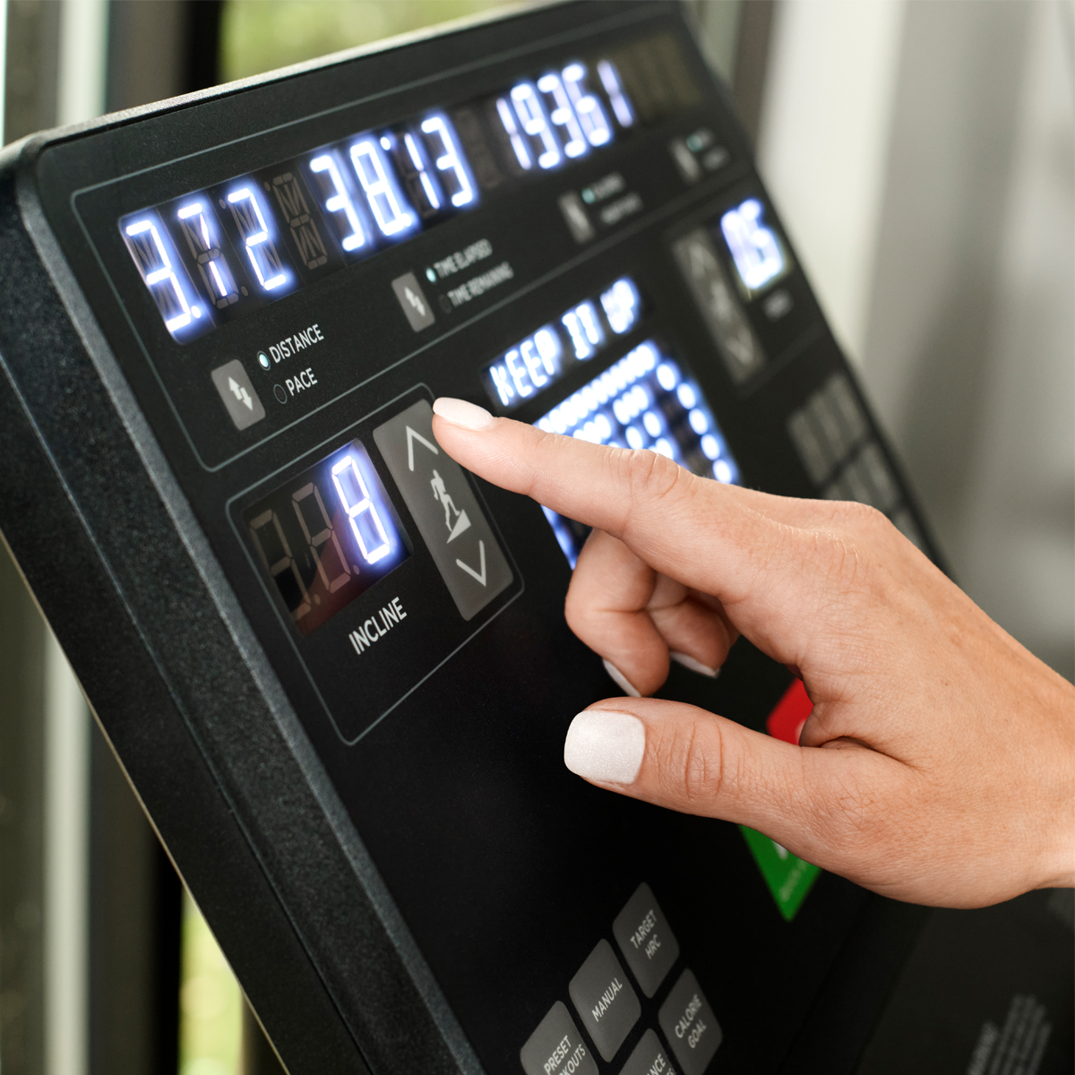 A close-up of a persons hand pressing the incline button on a treadmill console, with digital displays showing workout information like distance, time, and speed.