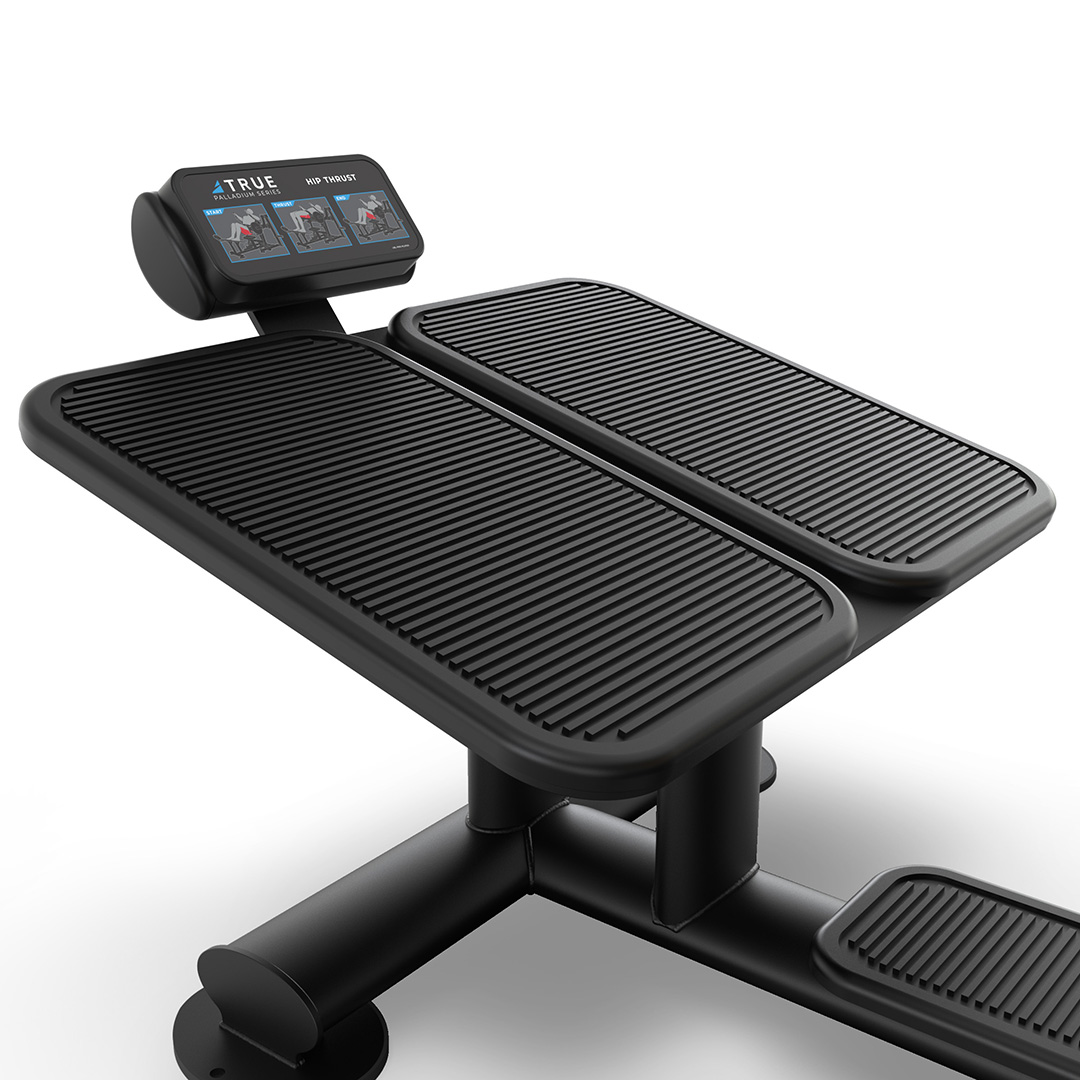 A close-up of a modern black fitness machine with two ribbed foot platforms and a digital display screen showing workout data. The design is sleek with sturdy support bars on a white background.