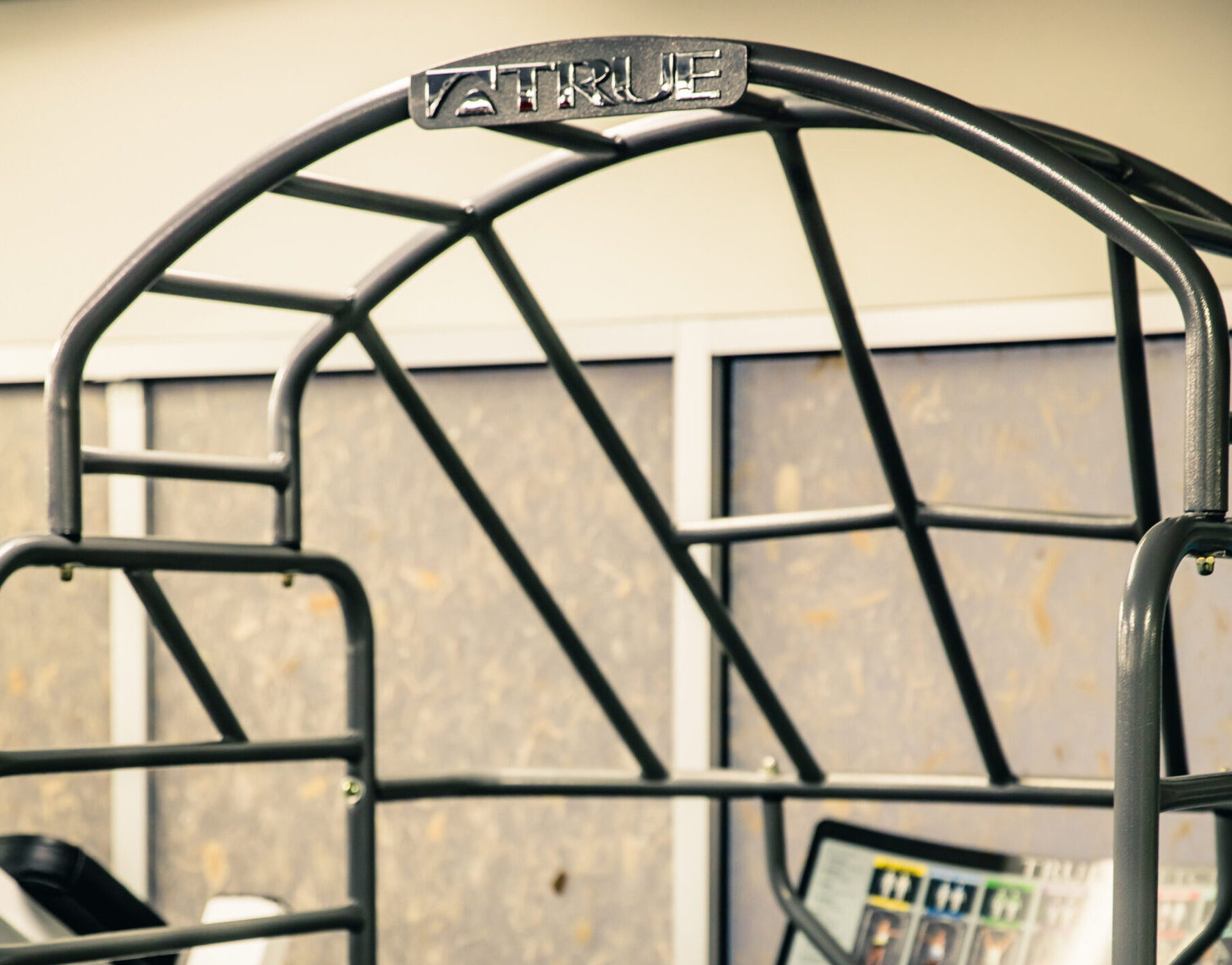 Close-up of a sturdy metal frame with the brand name VETTRUE on a curved top bar, set indoors with a textured wall and some brochures or posters visible in the background.