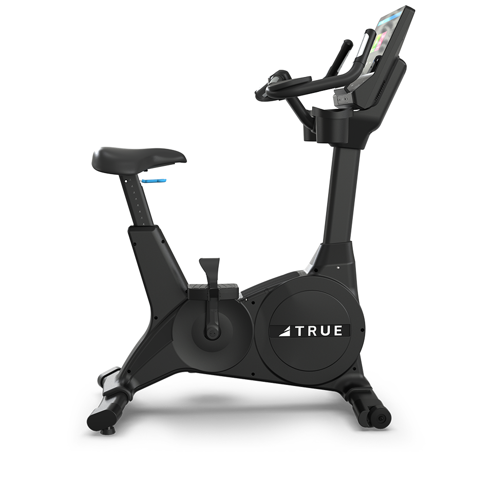 A stationary exercise bike with a digital display screen and adjustable seat, labeled “TRUE,” shown from the side against a plain white background.