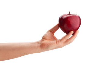 A hand with a light skin tone is holding a shiny red apple against a white background.