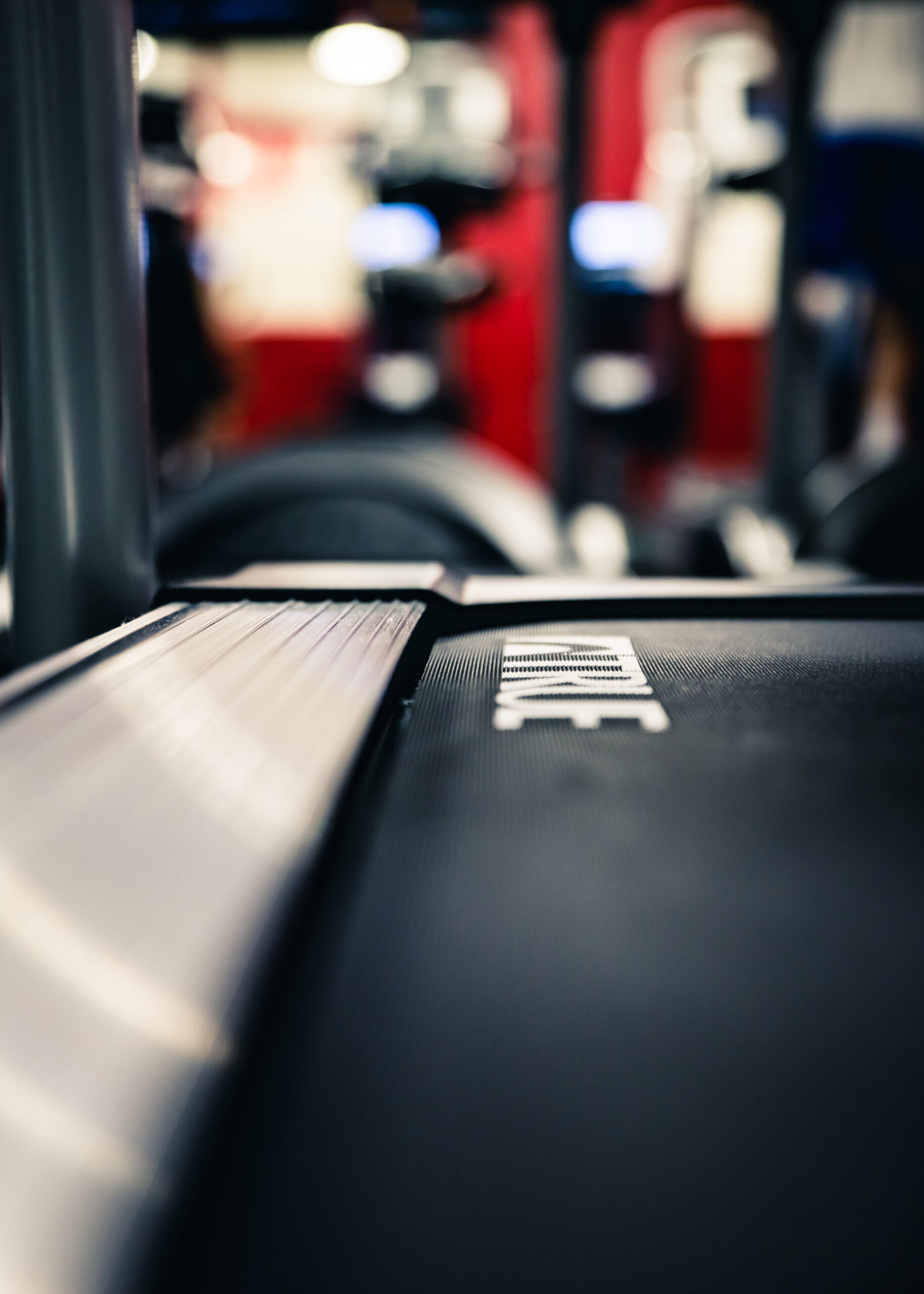 Close-up of a treadmill belt with blurred gym equipment and red walls in the background, creating a focused and athletic atmosphere.