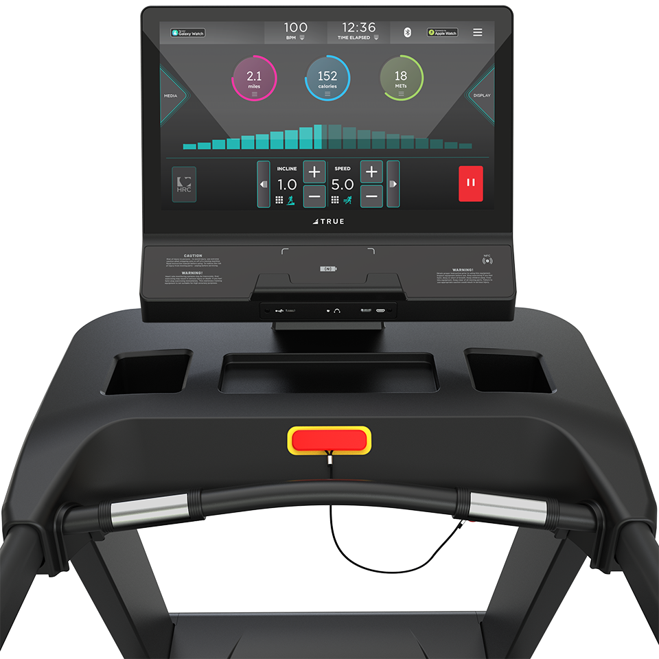 A close-up view of a treadmill console displaying workout data, including speed, distance, and time, with various control buttons and slots for holding items.